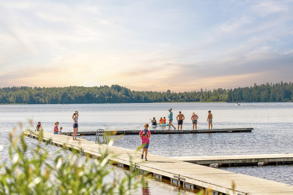 Badbrygga vid en sjo i kvallsljus med badande i vattnet