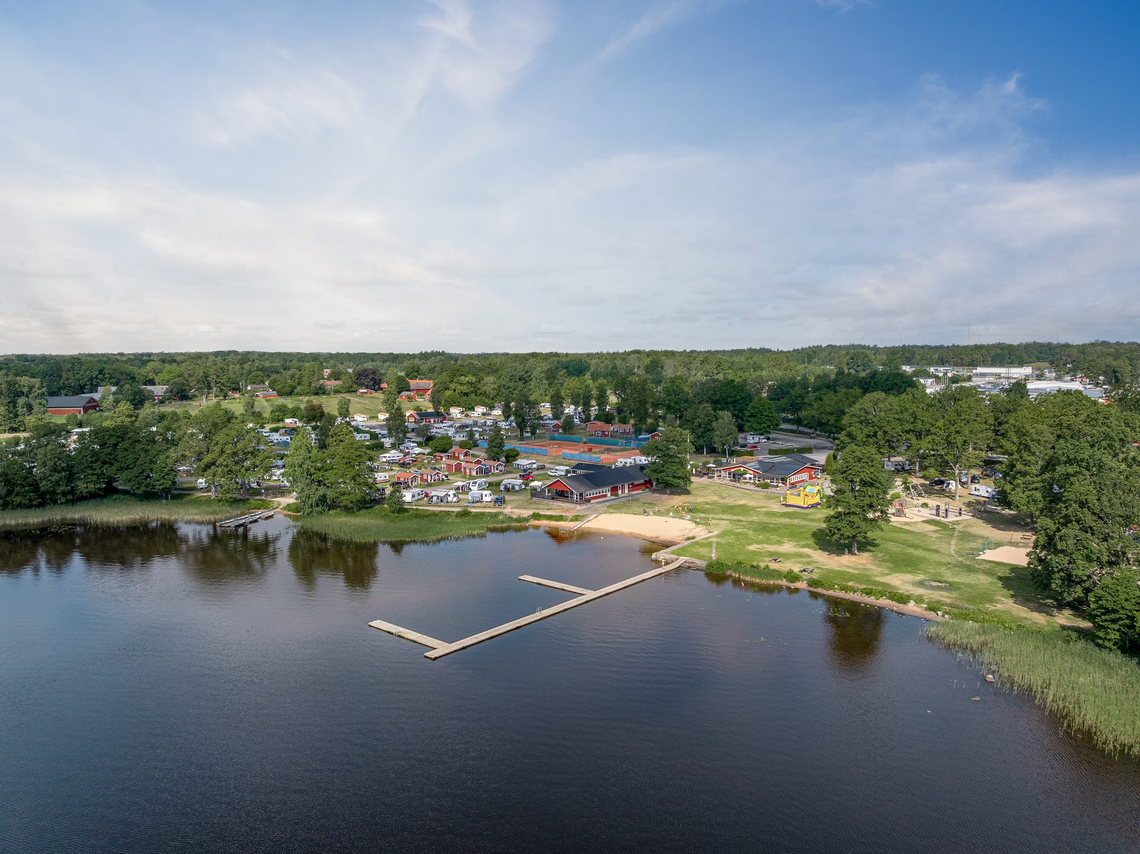 Dronbild over en campinganlaggning vid sjon med badbrygga och stugor